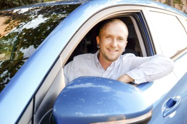 Direksiyon simidi, onun yeni Karayip Mavisi sürüş test araba oturan genç yakışıklı bir iş adamı. Aracını, gülümseyen adam newely satın alınan otomobil ile memnun. Portre, yakın çekim, arka plan