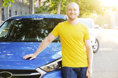 Sarı tişört onun yeni Karayip mavi araba eğilerek genç adam gülümseyen portresi. Yakışıklı erkek otomobil memnun yüz ifadesi ile yakın duran gündelik kıyafeti uygun. Alan arka plan kopyalama