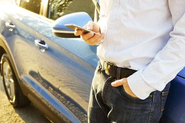 Smartphone kullanarak genç adam onun yeni Karayip mavi araba, eğilerek mavi gömlek resmi ware. Boş ekran cep telefonu elinde tutan bir erkek. GPS navigasyon kavramı. Yakın çekim, uzay, arka plan kopya.