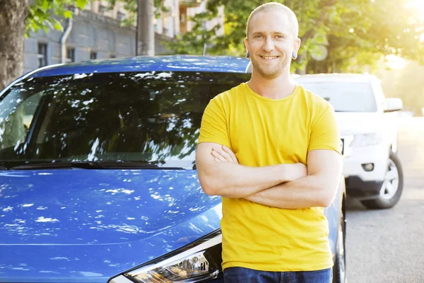 Sarı tişört onun yeni Karayip mavi araba eğilerek genç adam gülümseyen portresi. Yakışıklı erkek otomobil memnun yüz ifadesi ile yakın duran gündelik kıyafeti uygun. Alan arka plan kopyalama