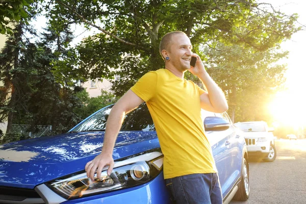 Sarı tişört yeni onun Karayip mavi araba eğilerek telefonda konuşurken genç adam. Yakışıklı erkek otomobil duran, smartphone kullanarak rahat kıyafetle uygun. Kopyalama alanı, arka plan, günbatımı.