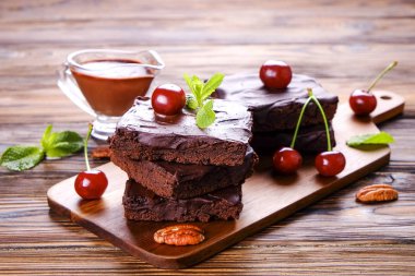 Ev yapımı kek kare parçaları, Yapıştır, kiraz ve pekan fındık ahşap masa üzerinde koyu çikolata yayıldı. Yüksek kalorili pasta. Kakao tatlılar, şekil için kötü dayalı. Yakın çekim, uzay arka plan, üstten görünüm Kopyala.