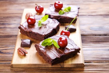 Ev yapımı kek kare parçaları, Yapıştır, kiraz ve pekan fındık ahşap masa üzerinde koyu çikolata yayıldı. Yüksek kalorili pasta. Kakao tatlılar, şekil için kötü dayalı. Yakın çekim, uzay arka plan, üstten görünüm Kopyala.