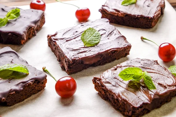 Koyu çikolata yayılması ile ev yapımı kek kare parçalar yapıştırın, beyaz masa üstü tarihinde kirazlı ve nane yaprakları. Yüksek kalorili pasta. Kakao tatlılar, şekil için kötü dayalı. Yakın, arka plan, top görünümü.