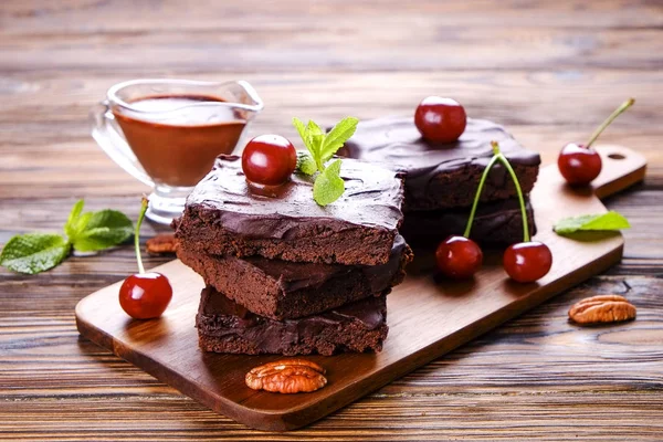 Ev yapımı kek kare parçaları, Yapıştır, kiraz ve pekan fındık ahşap masa üzerinde koyu çikolata yayıldı. Yüksek kalorili pasta. Kakao tatlılar, şekil için kötü dayalı. Yakın çekim, uzay arka plan, üstten görünüm Kopyala.