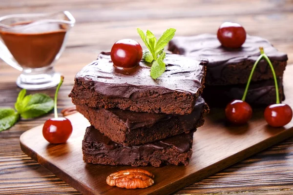 Ev yapımı kek kare parçaları, Yapıştır, kiraz ve pekan fındık ahşap masa üzerinde koyu çikolata yayıldı. Yüksek kalorili pasta. Kakao tatlılar, şekil için kötü dayalı. Yakın çekim, uzay arka plan, üstten görünüm Kopyala.