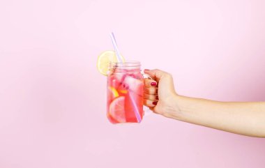 Taze tutan genç kadın el narenciye çilek limonata sıkılmış. Mason kavanoza soğuk kokteyl, limon, portakal, limon ve nane yaprakları dolu kadın var. Pembe bir arka plan, kopya alanı, yakın çekim.