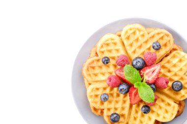 Çeşitli çilek karışımı, çilek, böğürtlen, ahududu ile kalp şekli Belçika Waffle ve nane yaprağı beyaz seramik plaka üzerinde kırmızı kuş üzümü süslenmiş. Yakın çekim, kopya alanı, arka plan, üstten görünüm.