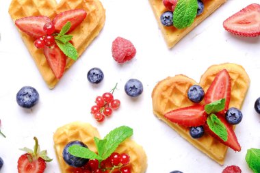 Çeşitli çilek karışımı, çilek, böğürtlen, ahududu ile kalp şekli Belçika Waffle ve nane yaprağı beyaz seramik plaka üzerinde kırmızı kuş üzümü süslenmiş. Yakın çekim, kopya alanı, arka plan, üstten görünüm.