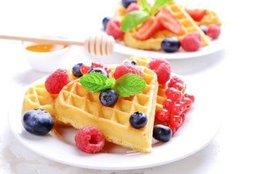 Çeşitli çilek karışımı, çilek, böğürtlen, ahududu ile kalp şekli Belçika Waffle ve nane yaprağı beyaz seramik plaka üzerinde kırmızı kuş üzümü süslenmiş. Yakın çekim, kopya alanı, arka plan, üstten görünüm.