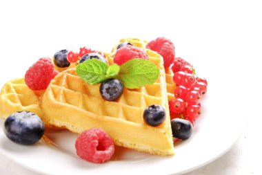Çeşitli çilek karışımı, çilek, böğürtlen, ahududu ile kalp şekli Belçika Waffle ve nane yaprağı beyaz seramik plaka üzerinde kırmızı kuş üzümü süslenmiş. Yakın çekim, kopya alanı, arka plan, üstten görünüm.