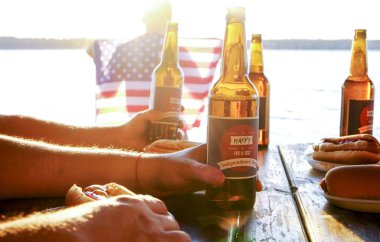 4 Temmuz kutlama parti, Genç Erkekler ellerini tutarak bira şişesi, tatil etiket tasarımı, mutlu bağımsızlık günü, hot dog, hardal, ketçap. Amerikan bayrağı, nehir rekreasyon alanı. Yakın çekim, arka plan