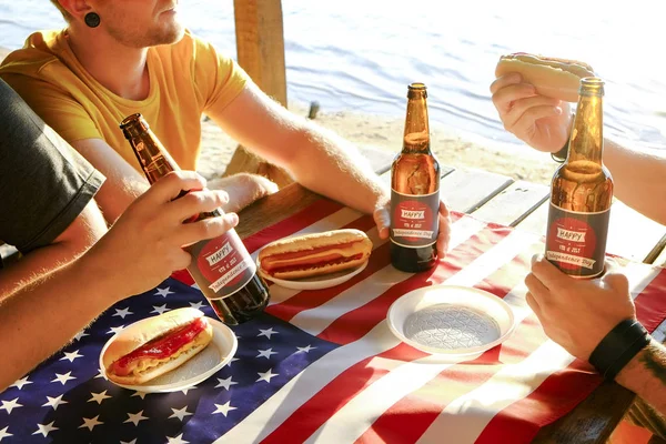 4th of July celebration party, young men hands holding beer bottle, holiday label design, Happy Independence day, hot dog, mustard, catchup. American flag, river recreation area. Close up, background