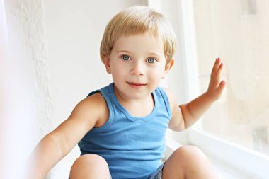 Pencere pervazına, perdenin arkasındaki saklambaç oynamaktan oturan sevimli küçük sarışın çocuk. Eğlenceli, gülümseyen ve gülen olan mutlu çok güzel üç yaşındaki çocuğun portresi. Arka plan, yakın çekim, alanı Kopyala.