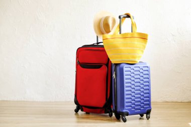 Kırmızı tekstil çanta ve mavi sert kabuklu Bagaj, genişletilmiş teleskopik kolu, hasır şapka, sarı plaj çantası, dekoratif doku duvar arka plan beyaz. Çiftler yolculuk kavramı çekilmek. Yakın çekim, alanı Kopyala.