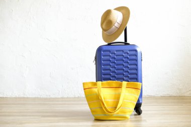 Tek mavi plastik sert kabuklu Bagaj kadın hasır şapka asılı ile genişletilmiş teleskop sapı ve sarı plaj çantası. Tatil gezisi için hazırlanmış bir bavul. Beyaz duvar arka plan, kopya alanı.
