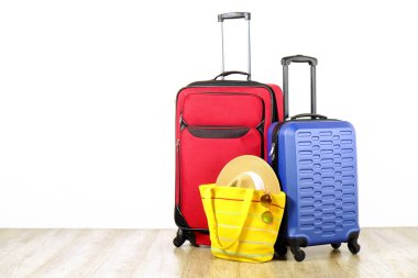 Kırmızı tekstil çanta ve mavi sert kabuklu Bagaj, genişletilmiş teleskopik kolu, hasır şapka, sarı plaj çantası, güneş gözlüğü, beyaz duvar arka plan yansıyor. Çiftler yolculuk kavramı çekilmek. Yakın çekim, alanı Kopyala.