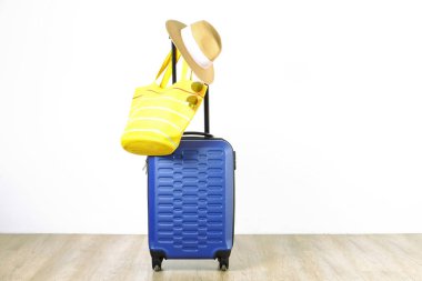 Tek mavi plastik sert kabuklu Bagaj kadın hasır şapka asılı ile genişletilmiş teleskopik kolu, sarı plaj çantası, güneş gözlüğü. Tatil gezisi için hazırlanmış bir bavul. Beyaz arka plan, kopya alanı