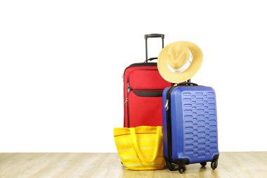 Kırmızı tekstil çanta ve mavi sert kabuklu Bagaj ile genişletilmiş teleskopik kolu, hasır şapka, ahşap zemin, beyaz duvar zemin üzerine sarı plaj çantası. Çiftler yolculuk kavramı çekilmek. Yakın çekim, alanı Kopyala