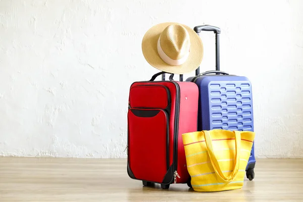 Red textile suitcase & blue hard shell luggage, extended telescopic handle, straw hat, yellow beach bag, white decorative texture wall background. Couples retreat trip concept. Close up, copy space.