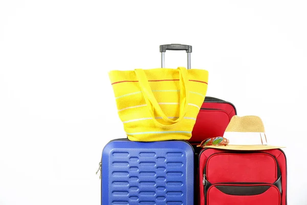 Three suitcases, red textile & blue hard shell luggage, extended telescopic handle, straw hat, beach bag, mirrored sunglasses, white wall background. Couples retreat trip concept. Close up, copy space