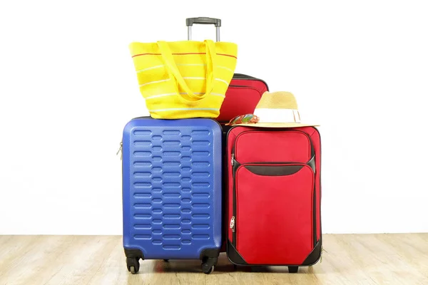 Three suitcases, red textile & blue hard shell luggage, extended telescopic handle, straw hat, beach bag, mirrored sunglasses, white wall background. Couples retreat trip concept. Close up, copy space