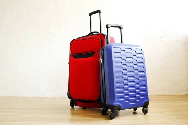 Red textile suitcase & blue hard shell luggage with extended telescopic handle up on wooden floor, white wall background. Couples retreat trip concept. Packed traveling baggages. Close up, copy space.