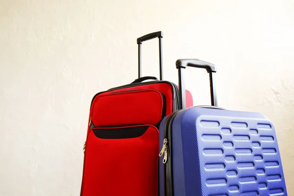 Red textile suitcase & blue hard shell luggage, extended telescopic handle up, white decorative texture wall background. Couples retreat trip concept. Packed traveling baggages. Close up, copy space.