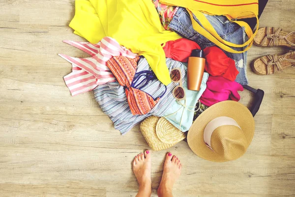 Open suitcase with pile of unfolded clothing on the floor. Woman packing for tropical vacation concept. Multiple unpacked female clothing items prepared for travel. Background, close up, copy space.