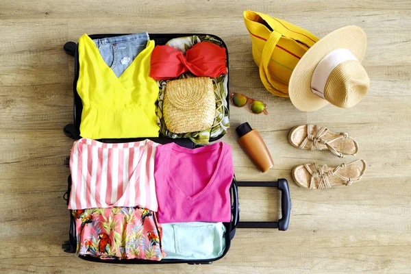 Open suitcase fully packed with folded women\'s clothing and accessories on the floor. Woman packing for tropical vacation concept. Female luggage w/ things. Background, close up, copy space, top view.