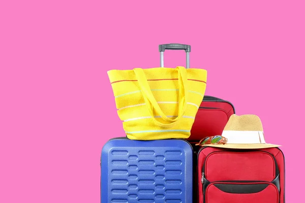 Three suitcases, red textile & blue hard shell luggage, extended telescopic handle, straw hat, beach bag, mirrored sunglasses, pink wall background. Family trip concept. Close up, copy space