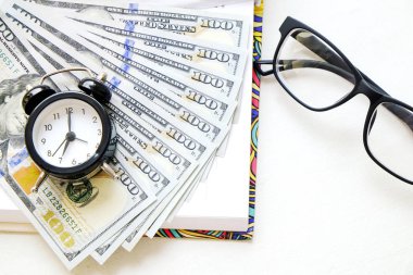 Zaman ve para yönetimi kavramı. Boş defter, çalar saat, kalem, hipster gözlük siyah çerçeve, birden fazla yüz dolar faturaları paketi açın. Arka plan beyaz boşluk kopya, yakın çekim, yat.