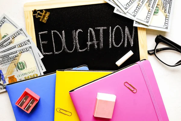 Investing money in expensive education, college tuition & fees concept. Pack of new one hundred dollar bills, notebooks, school supplies, black chalk board. Background, copy space, close up, flat lay
