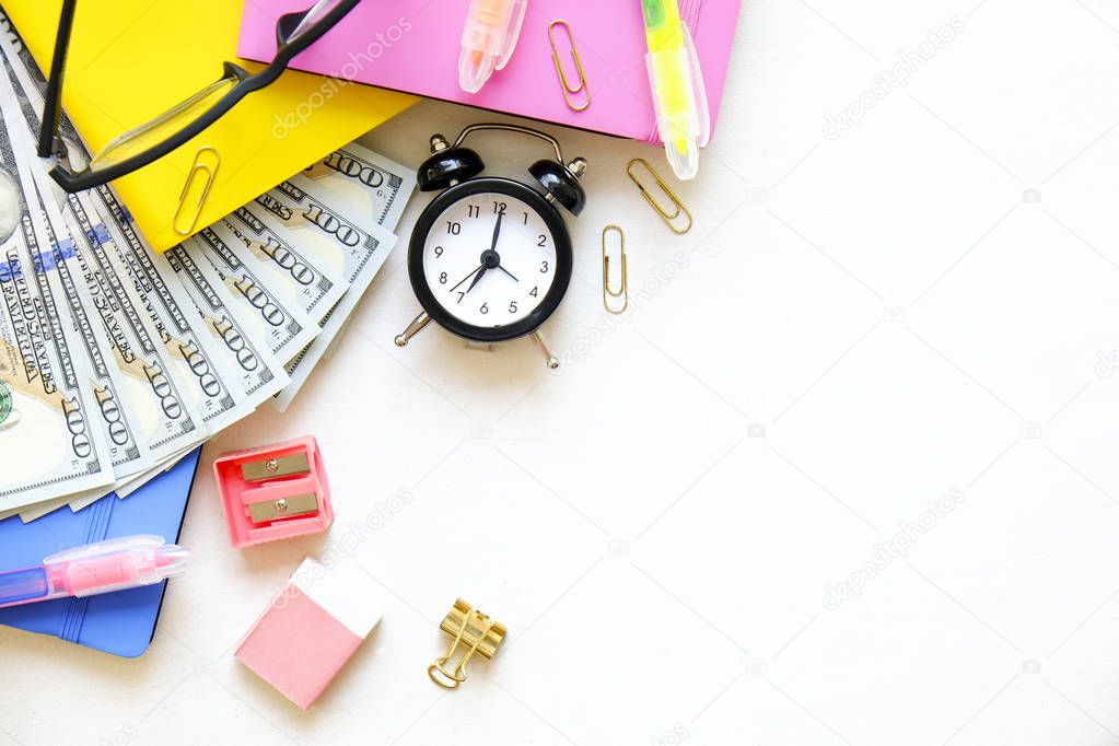 Investing time & money in expensive education, college tuition & fees concept. Pack of new one hundred dollar bills, notebooks, school supplies, alarm clock. Background, copy space, close up, flat lay