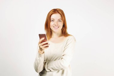 Cep telefonuyla gevşek beyaz gömlek giymiş smartphone ekranında, gülümseyen genç çekici doğal Kızıl saçlı bir kadın. Arka plan beyaz, uzay kopyalayın. Güzel erkek online dating app kavramı kullanma.