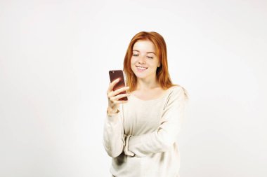 Cep telefonuyla gevşek beyaz gömlek giymiş smartphone ekranında, gülümseyen genç çekici doğal Kızıl saçlı bir kadın. Arka plan beyaz, uzay kopyalayın. Güzel erkek online dating app kavramı kullanma.