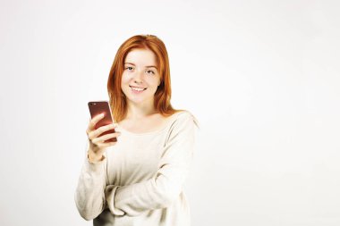 Cep telefonuyla gevşek beyaz gömlek giymiş smartphone ekranında, gülümseyen genç çekici doğal Kızıl saçlı bir kadın. Arka plan beyaz, uzay kopyalayın. Güzel erkek online dating app kavramı kullanma.