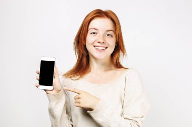 Boş ekran smartphone gösterilen geniş mükemmel ile gülümseyen genç güzel doğal kırmızı baş kadın. Çekici kadın parmağı kopya alan arka plan w / Mobil cep telefonu sergilenen işaret