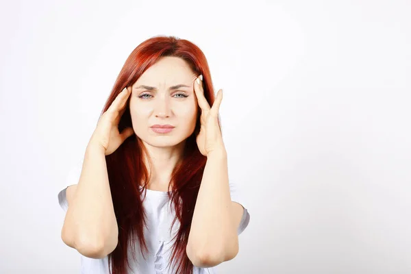 Beautiful redheaded young woman experiencing severe migraine writhing with pain. Pretty female suffering from head ache. Nonverbal behavior, body language. White background, close up, copy space.