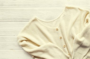 Moda kolay şık rahat tarzı büyük boyutlu kazak Beyaz ahşap dokulu masa arka plan üzerinde düğmeleri. Görünümü en iyi, yakın çekim, uzay kopyalayın. Şık kadın triko giyim ahşap yüzeyde yalan.