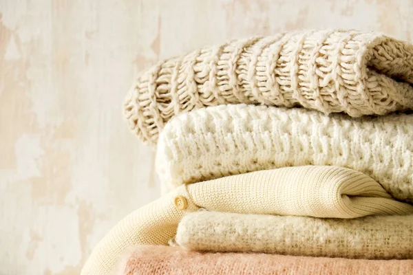 Bunch of knitted warm pastel color sweaters, different knitting patterns folded in messy stack on brown wooden table, grunged texture wall background. Fall winter season knitwear. Close up, copy space