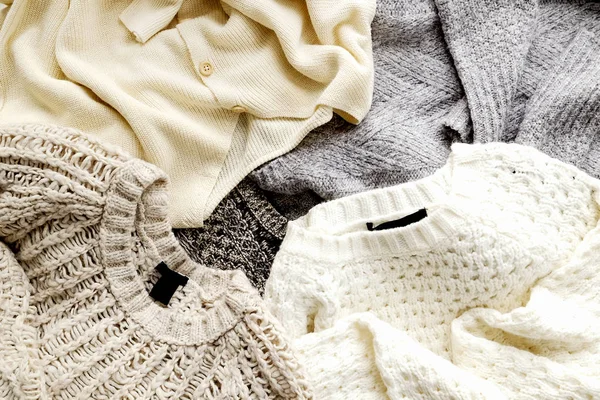 Bunch of knitted warm pastel color sweaters with different knitting patterns laid in messy pile, clearly visible texture. Stylish fall / winter season knitwear clothing. Close up, copy space, top view