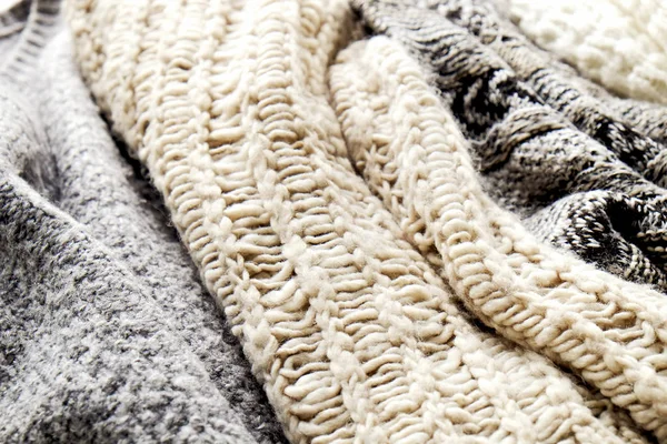 Bunch of knitted warm pastel color sweaters with different knitting patterns laid in messy pile, clearly visible texture. Stylish fall / winter season knitwear clothing. Close up, copy space, top view