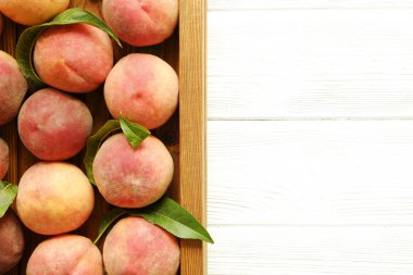 Beyaz ahşap dokulu masa üzerinde ip kulplu ahşap tepsi tepsi üzerinde yığın olgun organik şeftali demet. Yerli malı hasat yığın. Temiz kavramı yeme. Arka plan, görünümü top, yakın çekim, alanı Kopyala.