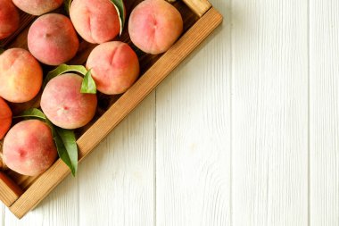 Beyaz ahşap dokulu masa üzerinde ip kulplu ahşap tepsi tepsi üzerinde yığın olgun organik şeftali demet. Yerli malı hasat yığın. Temiz kavramı yeme. Arka plan, görünümü top, yakın çekim, alanı Kopyala.