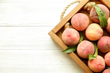 Beyaz ahşap dokulu masa üzerinde ip kulplu ahşap tepsi tepsi üzerinde yığın olgun organik şeftali demet. Yerli malı hasat yığın. Temiz kavramı yeme. Arka plan, görünümü top, yakın çekim, alanı Kopyala.