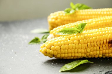 Yeşil fesleğen yaprakları ve karanlık taş masada tuz dekorasyon ile barbekü ateşe ızgara Mısır üç koçanı koydu. Temiz yemek alışkanlıkları kavramı. Arka plan, görünümü top, yakın çekim, yat, alanı Kopyala.