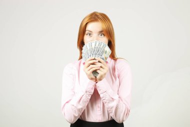 Avuç dolusu para demet yüz dolar faturaları fanı gibi holding ile yüzünü kaplayan genç güzel kızıl saçlı kadın. Tonla para heyecanlı çekici kadın var. Arka plan, kopya alanı, yakın çekim.