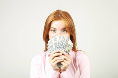 Avuç dolusu para demet yüz dolar faturaları fanı gibi holding ile yüzünü kaplayan genç güzel kızıl saçlı kadın. Tonla para heyecanlı çekici kadın var. Arka plan, kopya alanı, yakın çekim.
