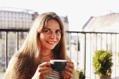 Çatı üstüne hipster kahve dükkanında oturmuş, sıcak içecek içme güzel ve genç birbayan. Çekici kadın sipping kapuçino fincan gülümseyen, İtalya kafe Teras. Arka plan, yakın çekim, alanı Kopyala.